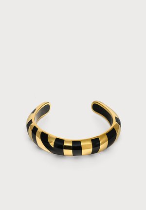 Bracelet manchette ouvert rayé or et noir avec une surface lisse et incurvée sur un fond uni clair.