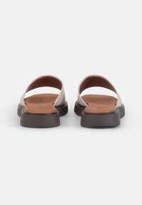 Beige slip-on shoes with a smooth leather upper. Features a flat brown sole and an open back, offering a minimalist design.