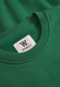 Green sweatshirt made of soft cotton, featuring a round neck, ribbed collar, and a label with a logo. Smooth texture with a solid color.