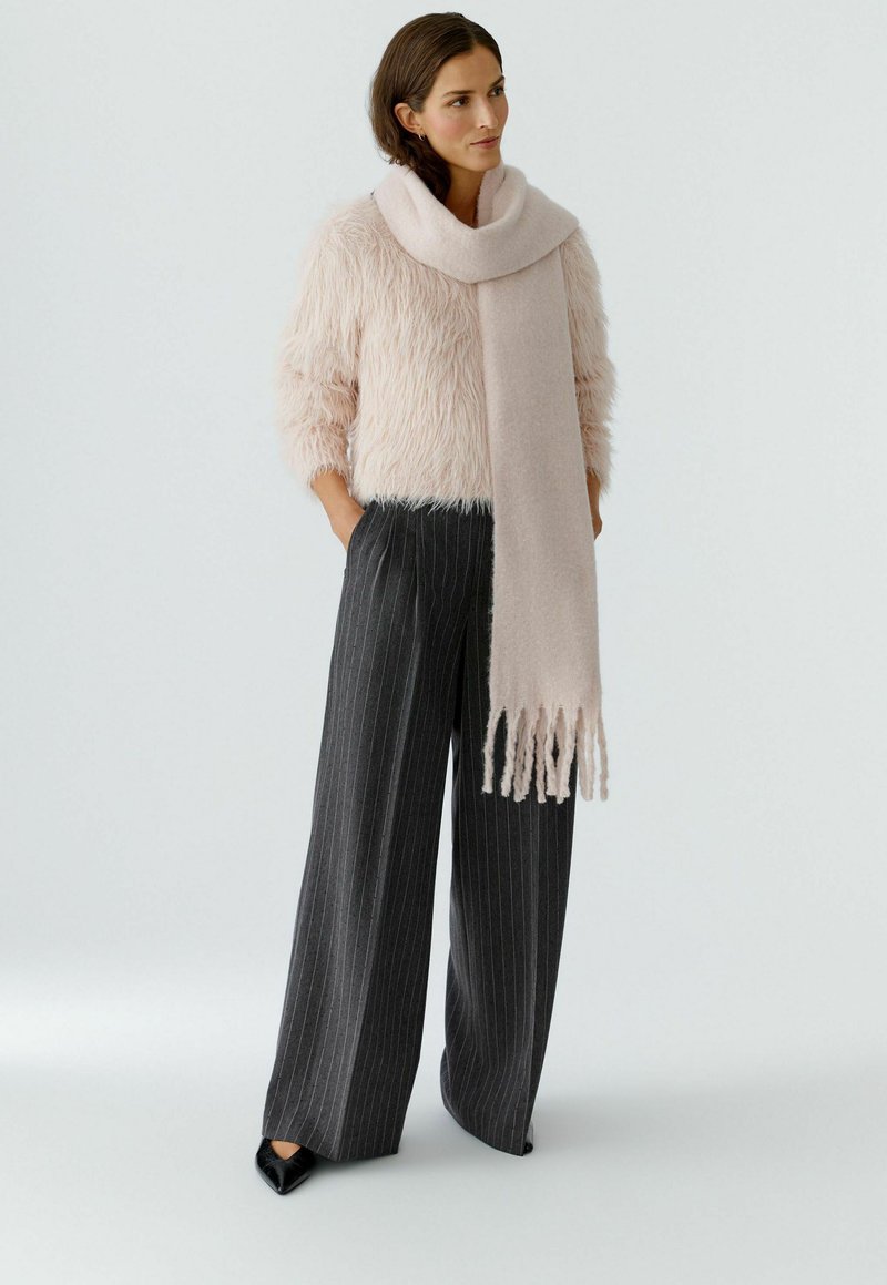 Helle rosa, flauschige Pullover, graue fein gestreifte, weit geschnittene Hose und ein passender heller rosa Schal mit Fransen. Schwarze spitze Schuhen.