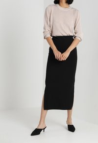 Svart, figurnära midikjol med hög slits; kombinerad med en lätt, texturerad rosaskimrande tröja och svarta klackskor med spetsig tå.