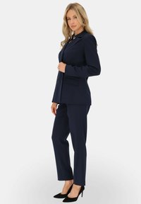 Granatowy, dopasowany garnitur z wyraźną marynarką z klapami i dopasowanymi spodniami o slim fit. Noszony z czarnymi szpilkami.