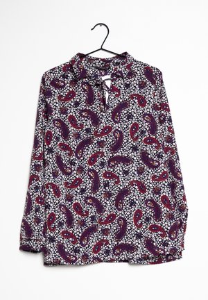 Bluse mit langen Ärmeln, gemustert mit lila, roten und weißen Paisley- und Blumenmotiven, hängt an einem schwarzen Kleiderbügel vor weißem Hintergrund.