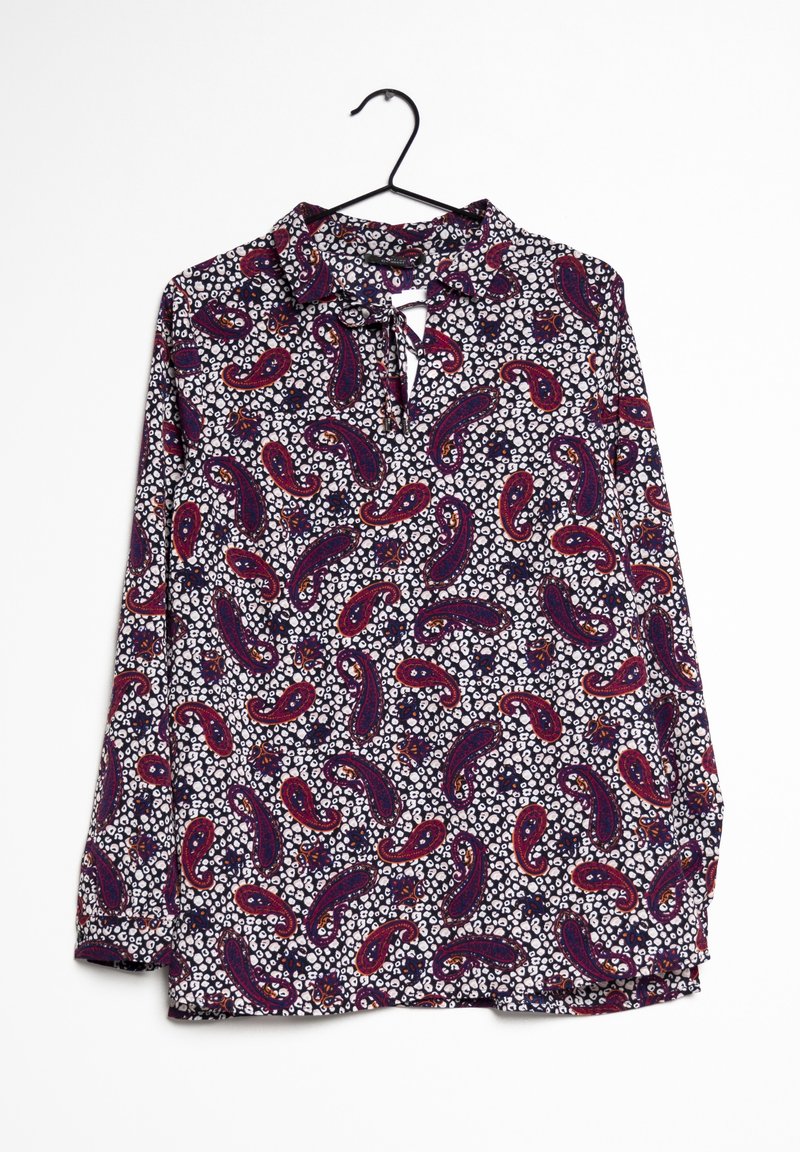 Blouse à manches longues avec motif cachemire et floral en violet, rouge et blanc, suspendue à un cintre noir sur fond blanc.
