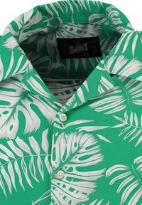 Korteboven, groene shirt met witte tropische bladerenpatronen, een knoopsluiting en kraag. Gemaakt van lichte stof. Maatlabel zichtbaar.