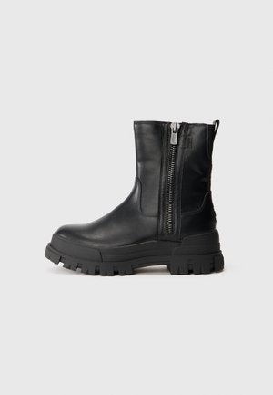 Bota de tornozelo em couro preto com sola de borracha robusta, fecho de zíper lateral e pega. Textura suave com um design elegante.