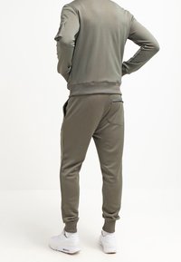 Tuta verde oliva con una texture liscia, caratterizzata da una felpa aderente e pantaloni a gamba affusolata, arricchita da tasche con zip e polsini a coste.