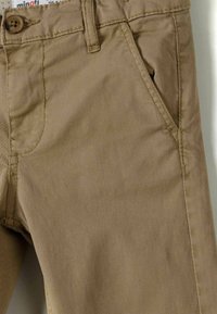 Pantalones de algodón beige con una textura suave, que cuentan con un cierre de un solo botón, trabillas para el cinturón y bolsillos laterales.