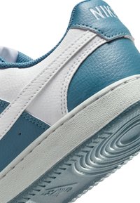 Le sneakers Nike presentano una tomaia in pelle blu e bianca, una superficie testurizzata, una suola in gomma bianca e un dettaglio di cucitura notevole.