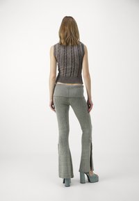 Top de punto sin mangas con un patrón de cadenas en marrón oscuro, combinado con pantalones de canalé grises con aberturas laterales, complementados con zapatos de plataforma chunky.