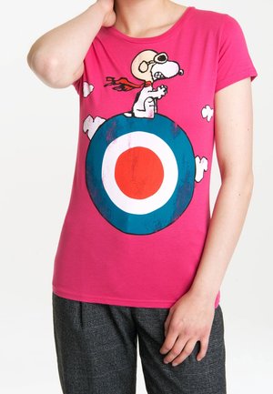 Persona con una camisa rosa con Snoopy en equipo de aviador sentado sobre un diseño de objetivo en azul, blanco y rojo, rodeado de pequeñas nubes blancas.