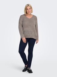 Beige knitted sweater with a V-neck and long sleeves, paired with dark blue slim-fit jeans and black chunky-soled shoes.