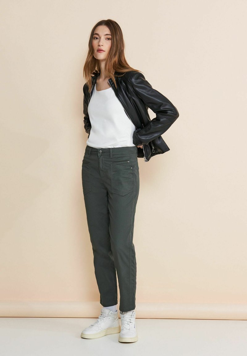 Svart läderjacka, vit linne, och mörkgröna byxor. Slim fit-byxor med framfickor. Vita sneakers kompletterar outfiten.