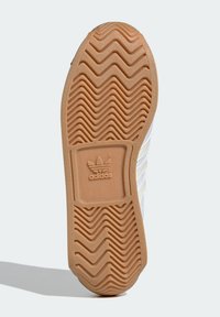 Gummi sula med zigzag-mönster, beige färg, med präglad logotyp. Slät yta med räfflad textur för grepp och dragkraft.