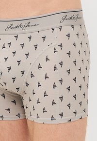 Graue Boxershorts aus weichem Stoff, mit kleinen schwarzen abstrakten Mustern und einem elastischen Bund mit Markenlogo.
