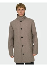 Cappotto marrone di lana con collo alto, cinque bottoni neri e tasche laterali; presenta un taglio dritto e una texture liscia.