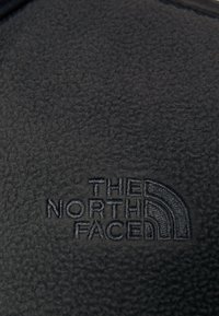 Tessuto felpato nero con logo embossato con il testo "THE NORTH FACE" e un design grafico a mezza cupola. Texture liscia.