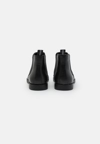 Botines de cuero negro con una textura suave, paneles laterales elásticos y tiradores en la parte trasera. Suelas de goma negra sólida.