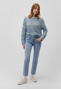 Gestreifter gestrickter Pullover in Blau und Grün mit lockerer Passform, kombiniert mit hellblauen geraden Jeans und weißen Sneakern mit strukturiertem Sohlen.