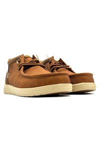 Chaussures en cuir marron avec une texture lisse, bout rond, semelle en caoutchouc crème et fermeture à lacets. Détail de logo visible sur le côté.