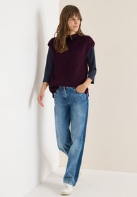 Neulemaa ilman hihnoja viininpunaisena, yhdistettynä sinisiin leveälahkeisiin farkkuihin. Teksturoitu kangas, sivuslitit ja rento valkoinen lenkkitossu.