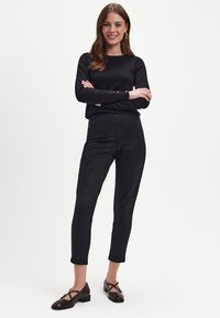 Czarna bluzka z długim rękawem, dopasowane czarne legginsy z zamszu, oraz ciemnobrązowe buty na niskim obcasie z krzyżującymi się paskami. Prosty design, gładka tekstura.