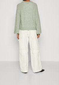 Světle zelený pletený svetr s uvolněným střihem a spadlými rameny, v kombinaci s krémovými širokými kalhotami s kapsami po stranách.