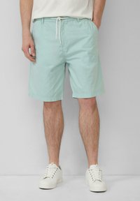 Helle mintgrüne Shorts aus Baumwolle, mit einem Kordelzugbund und seitlichen Taschen, ergänzt durch weiße Sneaker.