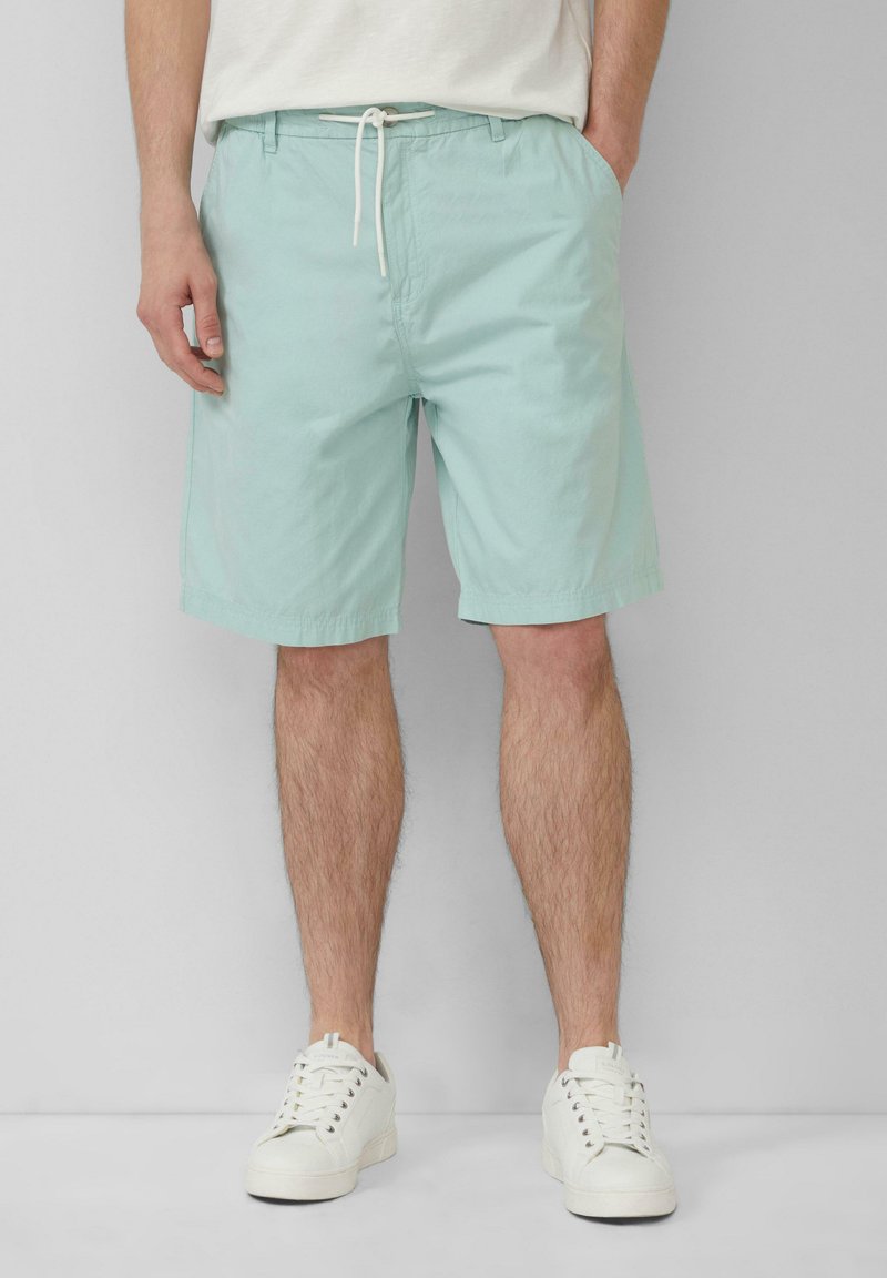 Helle mintgrüne Shorts aus Baumwolle, mit einem Kordelzugbund und seitlichen Taschen, ergänzt durch weiße Sneaker.