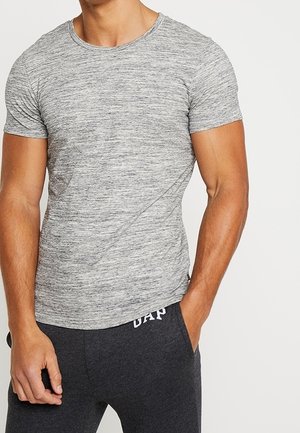T-shirt gris chiné à manches courtes et col rond, coupe ajustée. Porté avec un pantalon de survêtement gris foncé à cordon de serrage, orné d'un détail logo.