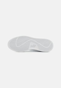 Suela de zapatilla blanca con un patrón de banda de lunares y un logo en relieve. El material parece ser goma con áreas suaves y texturizadas.
