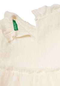 Vestido color crema con cuerpo de punto texturizado y falda de tul transparente. Presenta un escote con volantes y una etiqueta de United Colors of Benetton.