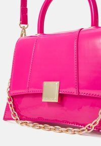 Sac à main en cuir verni rose vif avec poignée supérieure, fermoir carré doré et détail chaîne dorée sur fond blanc.