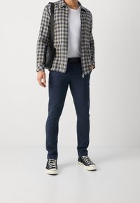 Kostkovaná bunda v námořnické modři a žluté přes bílé tričko, doplněná námořnickými chinos a černými teniskami. Součástí je černá kabelka přes rameno.