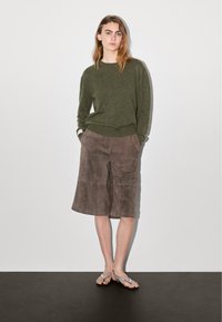 Maglione verde a maglia, pantaloni corti in suede marrone, infradito grigie. Il maglione presenta un collo rotondo e polsini a coste; i pantaloni corti sono lunghi fino al ginocchio e dotati di tasche laterali.
