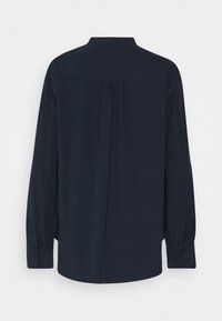 Maglietta blu navy a maniche lunghe con polsini abbottonati e pieghe sul retro, mostrata da dietro su uno sfondo bianco puro.