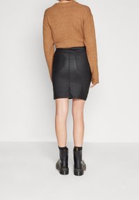 Svart denimkjol med bakfickor, hög midja och sömnadsdetaljer, tillsammans med en brun stickad tröja och svarta ankelstövlar.