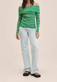 Haut côtelé rayé vert et rose, à épaules dénudées et manches longues, assorti à un jean bleu clair à jambes larges et des sandales compensées noires.