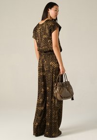 Jumpsuit marrone con motivo, maniche corte, vita elasticizzata e gambali larghi. Abbinato a una borsa lucida marrone.