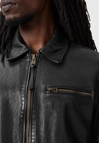 Black leather jacket with a collar, featuring a front zipper and a left chest pocket zippered pocket, has a smooth texture and minimal detailing.
