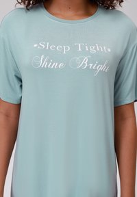 Ljusblå T-shirt i mjukt tyg, med vit text som säger "Sov Gott Skin Klar", kortärmad och med rund halsringning.
