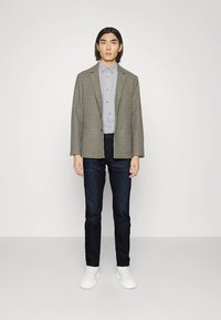 Hall kollažiriietusega bleiser, helehall nööbitav särk, tumedad teksad ja valged tossud. Sirged sääred ja lõdvestunud siluett.