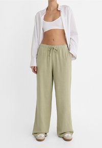 Lichtgroene, losse linnenmix broek met een elastische tailleband en een trekkoord. Draagt een witte crop top en shirt.
