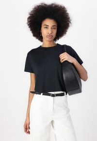Camiseta negra de manga corta en tejido suave, combinada con pantalones blancos de cintura alta y un bolso de hombro de cuero negro. Diseño simple.