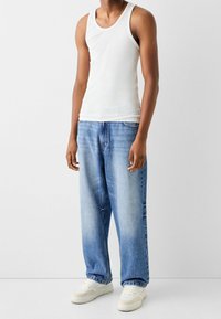 Vit bomullstopp i tank-stil, matchad med ljusblå, löst sittande denimjeans och vita sneakers, med en klassisk design med fem fickor.