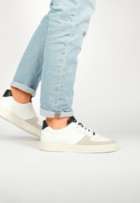 Bílé kožené tenisky s šedými semišovými akcenty, černou patní částí a bílou gumovou podrážkou. Nošeny s ohrnutými světle modrými džíny.