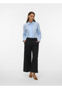 Camisa azul claro de botones con mangas largas, combinada con una corbata a juego y pantalones negros de pierna ancha de talle alto, junto con tacones marrones.