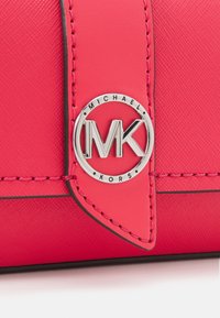 Borsa in pelle sintetica rosa brillante con dettagli cuciti e una placca rotonda in argento con il logo "MK" e il testo "Michael Kors".