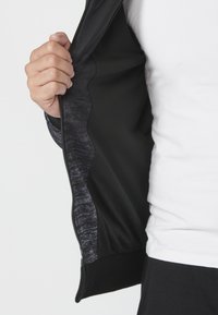 Čierna bundová mikina na zips s textúrovanou vnútornou vrstvou, zobrazená otvorená. Golier a manžety sú hladké a majú pevnú štruktúru.