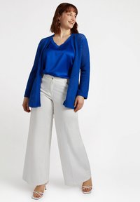 Blå öppen stickad cardigan över en blå satinblus, tillsammans med vita vida byxor och ljusa klackar med remmar. Släta texturer, livliga färger.